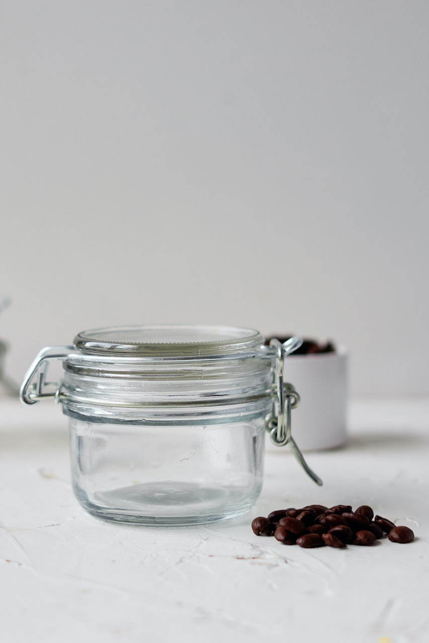 a small jar sitting on a white table with coffee beans in a pile sitting next to the jar