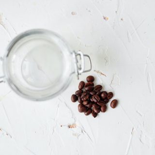 coffee beans sitting on a white table with an empty mason jar next to them