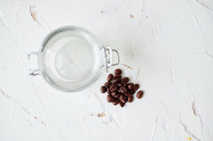 coffee beans sitting on a white table with an empty mason jar next to them