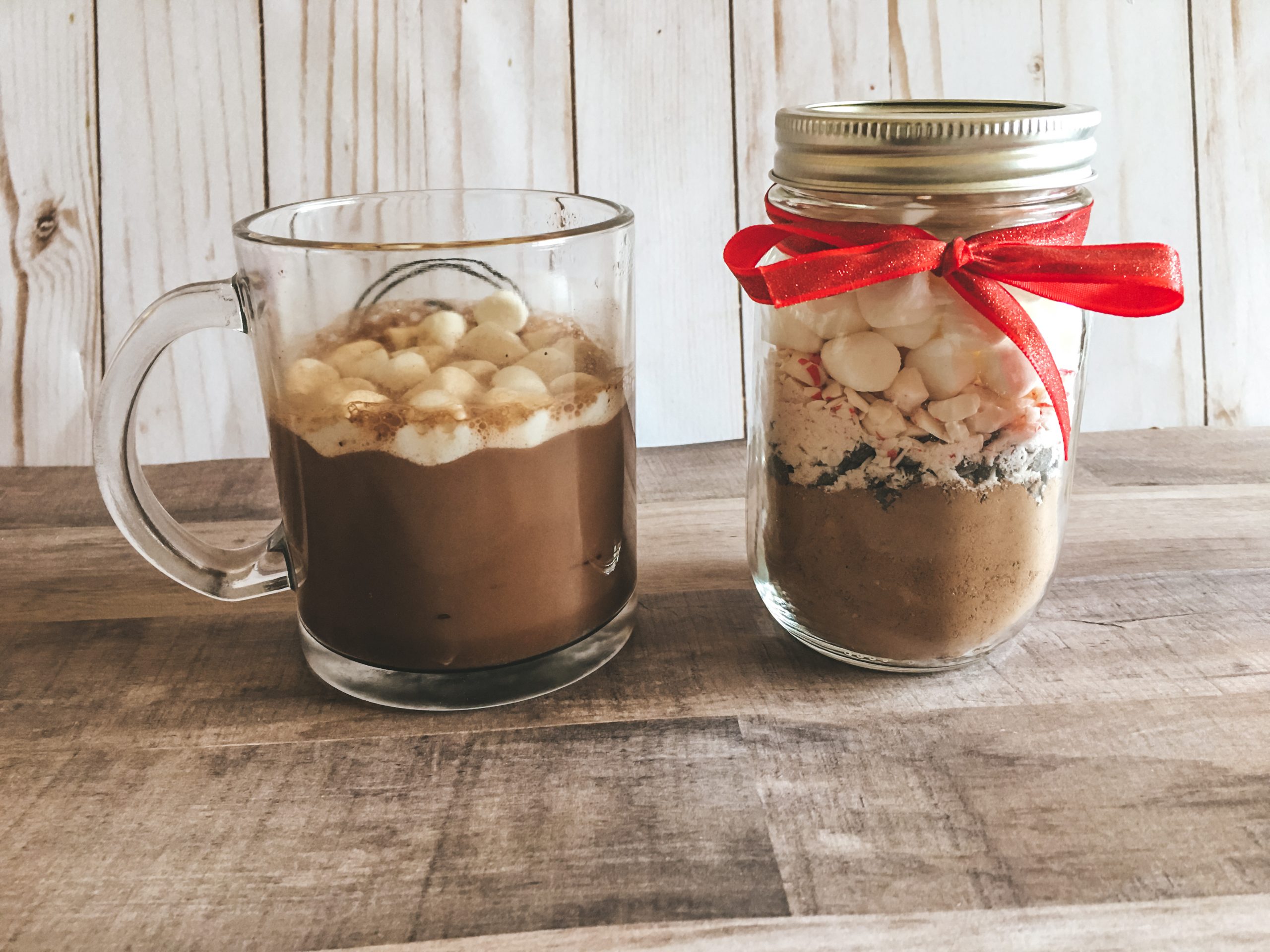 a mug filled with hot chooclate topped with mini marshmallows sitting next to a mason jar filled with mix as a gift