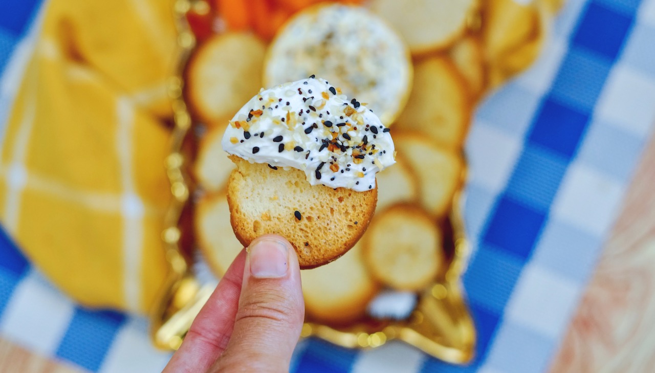 a hand holding a bagel chip covered with dip. Serving platter in background