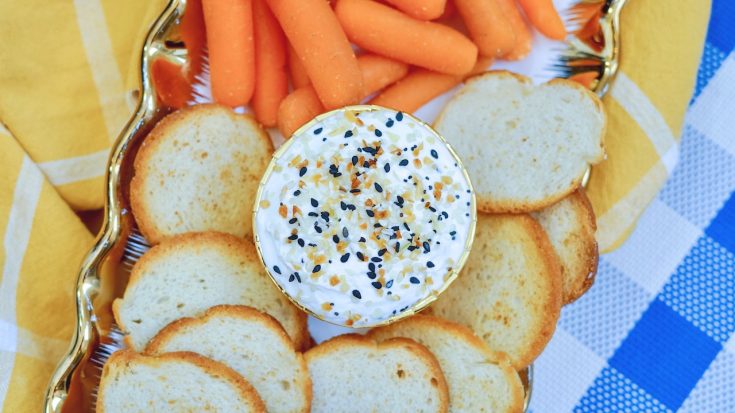 a bowl of dip surrounded by bagel chips and carrots