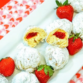 strawberry donut holes covered in powdered sugar sitting on a white plate with whole strawberries on top of a red and heart covered placemat