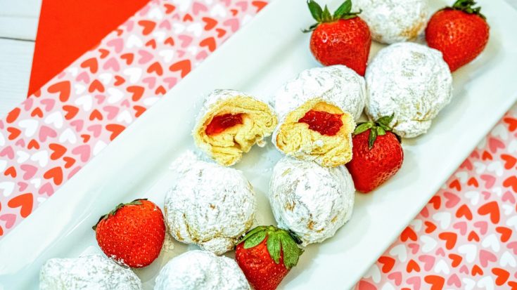 strawberry donut holes covered in powdered sugar sitting on a white plate with whole strawberries on top of a red and heart covered placemat