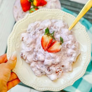 a plate filled with strawberry fluff topped with a sliced strawberry, being held with a golden spoon.