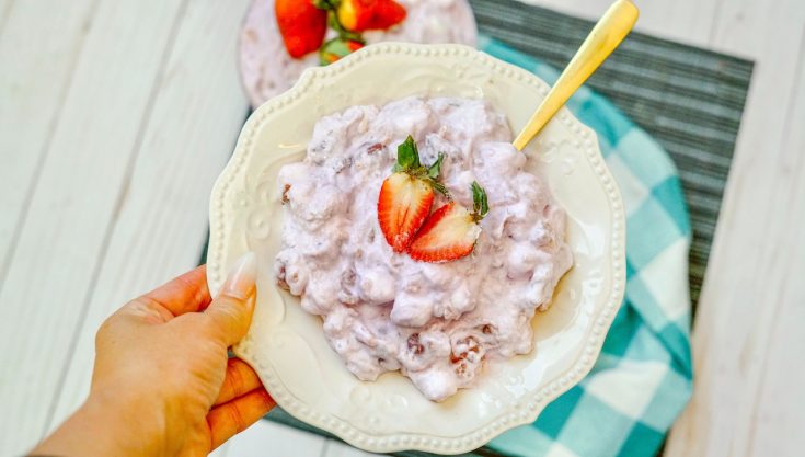 a plate filled with strawberry fluff topped with a sliced strawberry, being held with a golden spoon.