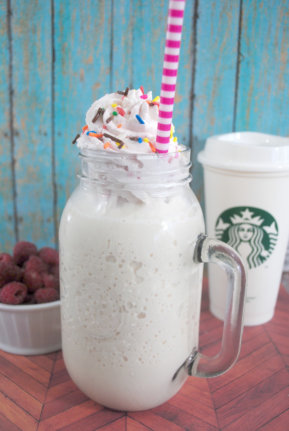 copycat Starbucks birthday cake frappuccino in a glass topped with whipped cream and sprinkles with a striped paper straw.