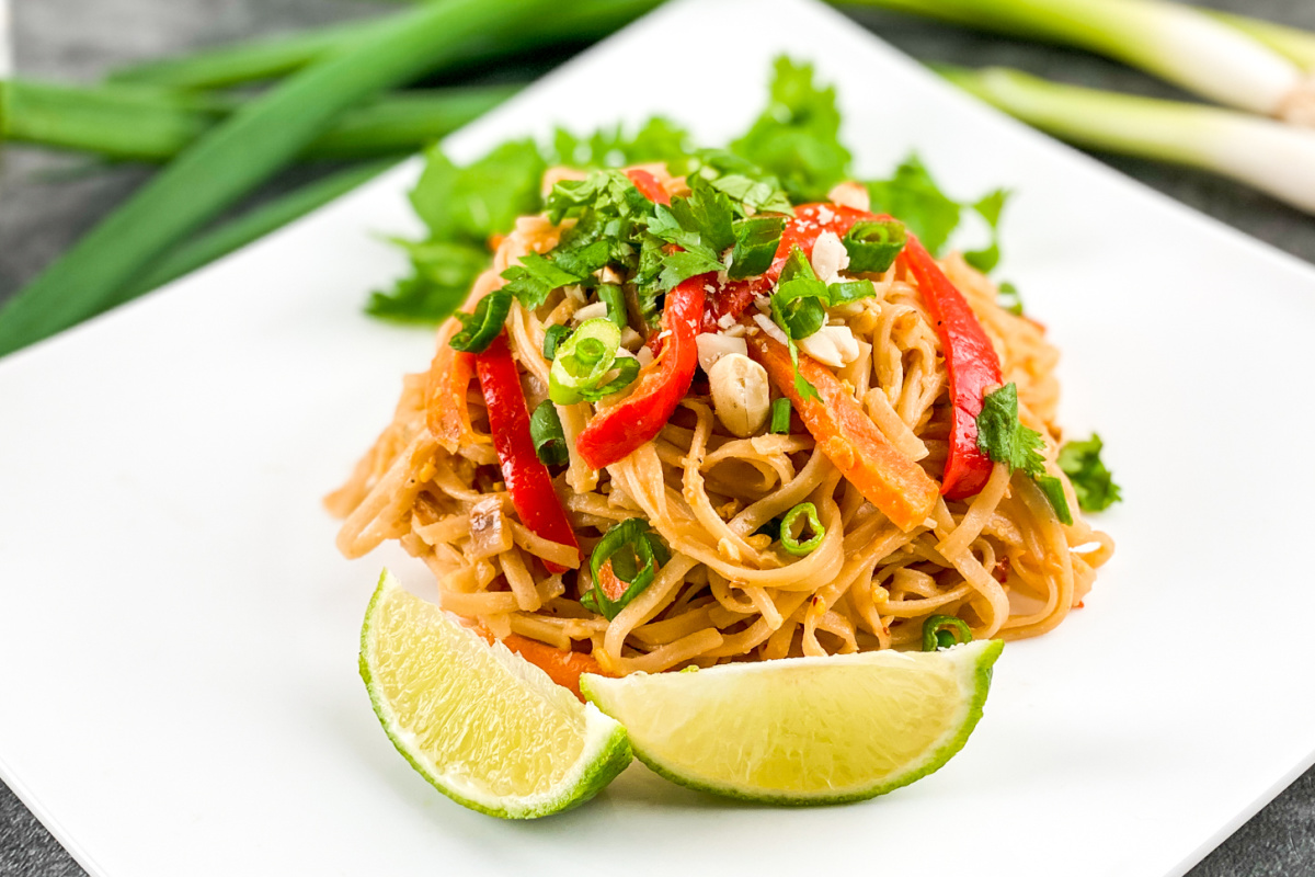 a plate of vegetable pad thai with limes