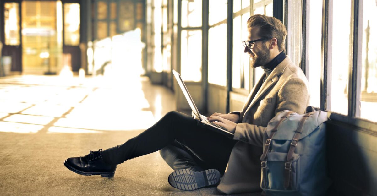 Man sitting by a window at a Budapest train station working on his laptop with sunlight streaming through