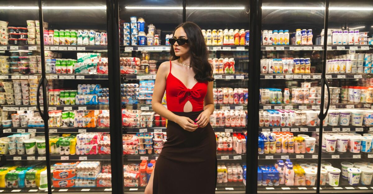Fashionable woman in sunglasses stands confidently in front of refrigerated groceries