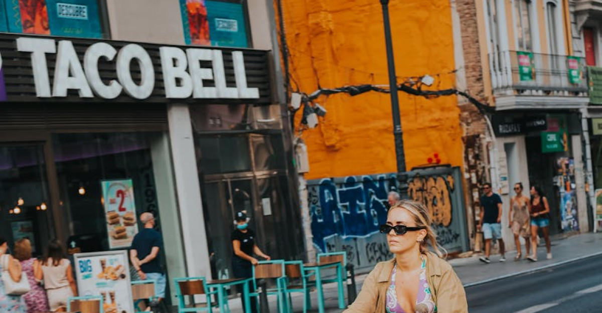 Woman on bicycle rides past Taco Bell in vibrant city street scene