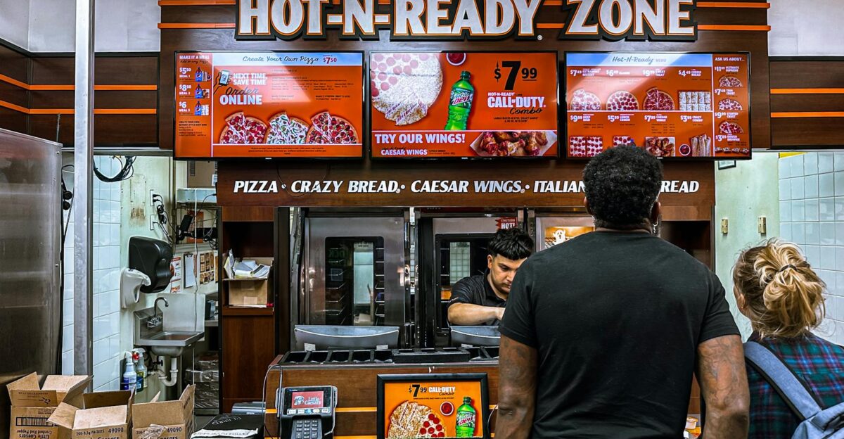 Busy fast food restaurant with customers ordering pizza at the counter under bright digital menu signage