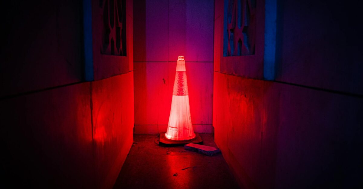A red neon-lit traffic cone emits a mysterious glow in a dark urban alleyway creating an enigmatic atmosphere