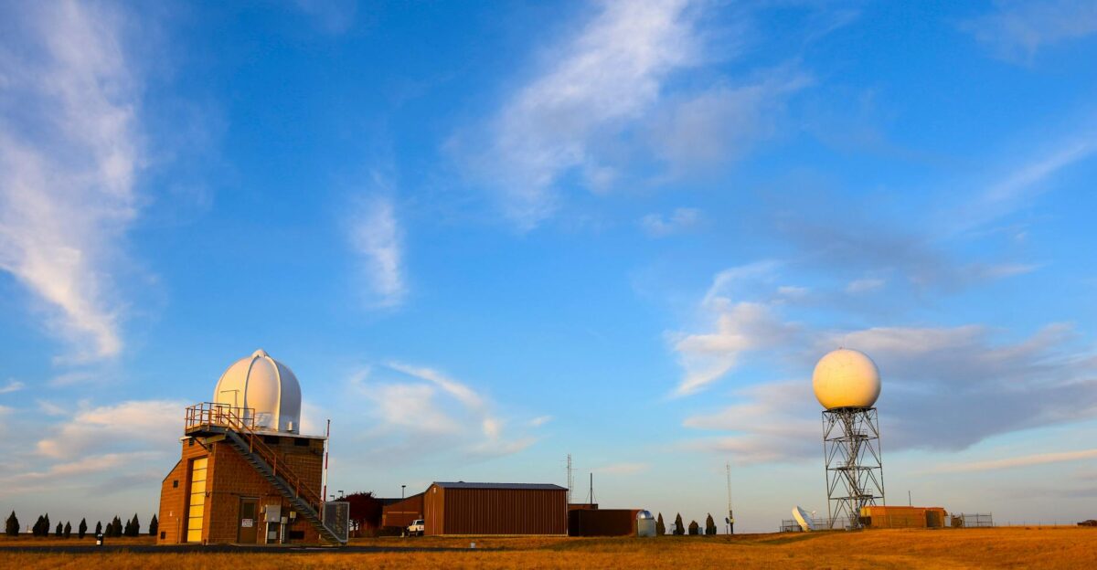 Weather radar station set in a field with a clear blue sky and scattered clouds showcasing meteorological technology