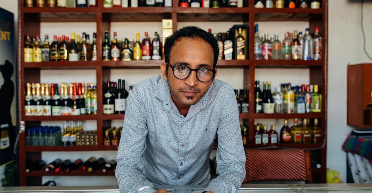 Man standing behind a counter in a liquor store filled shelves of wine bottles behind him
