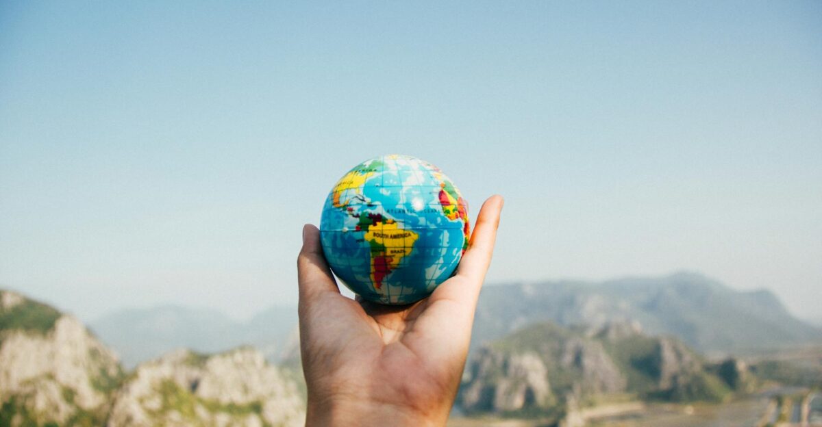 Hand holding a globe against a mountain background symbolizing travel and exploration