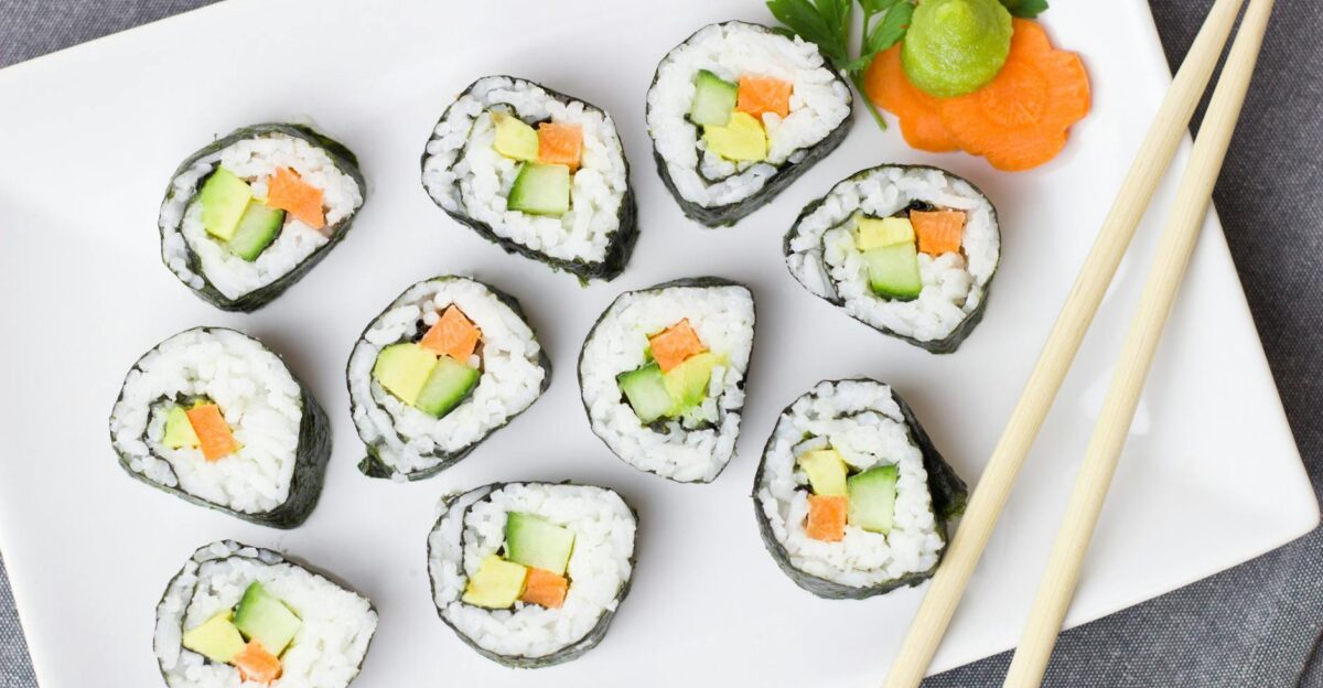 Top view of vegetable sushi rolls with chopsticks and wasabi on a white plate
