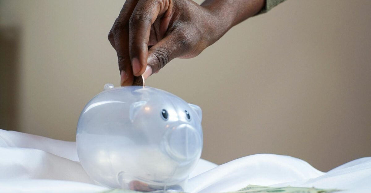 Close-up of a person s hand placing coins into a transparent piggy bank to save money