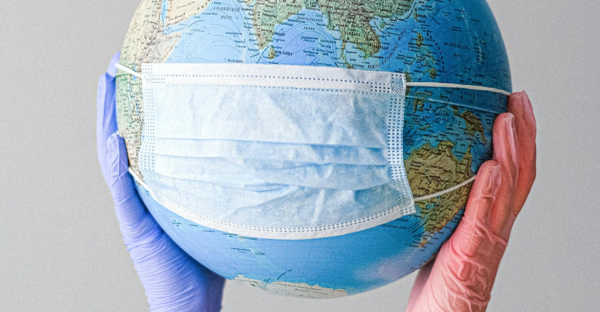 Hands in gloves holding a globe with a mask, symbolizing global health and pandemic protection.