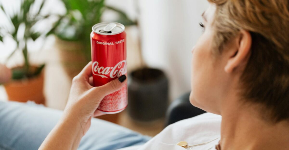 A woman in casual attire enjoys a soda while relaxing indoors surrounded by greenery