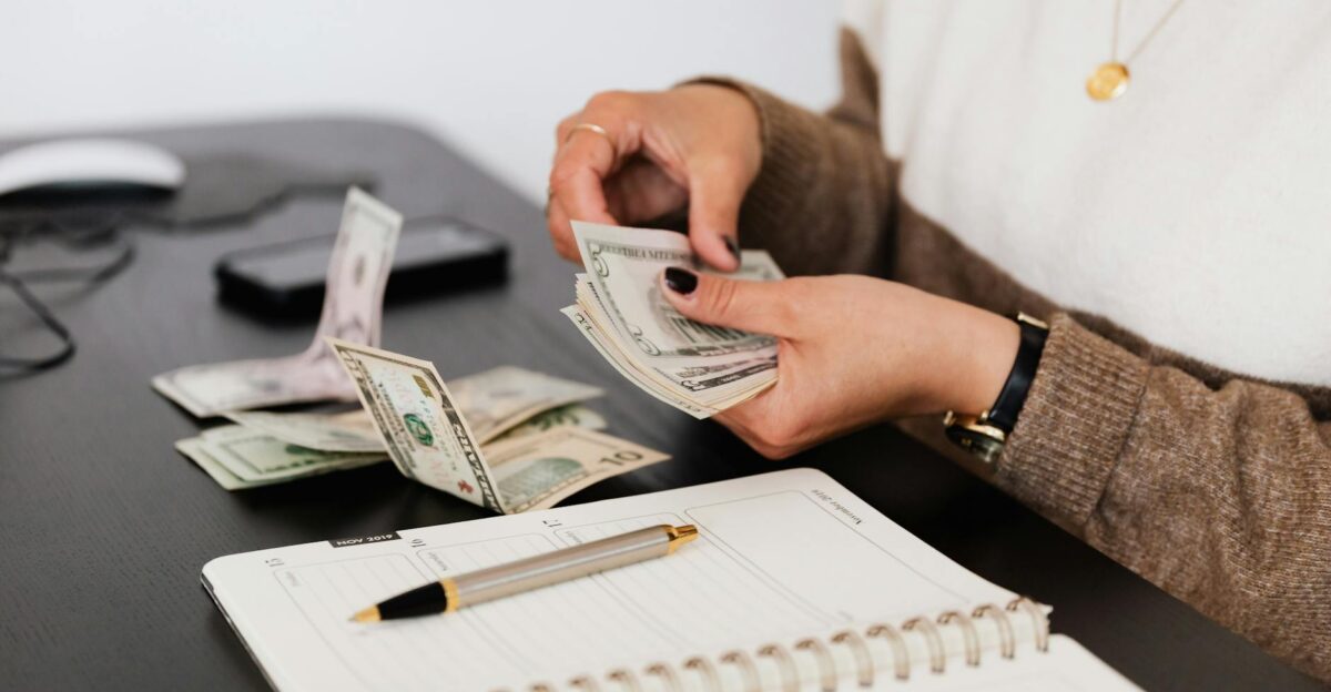 Close-up of person counting cash with notepad on desk indicating financial tasks