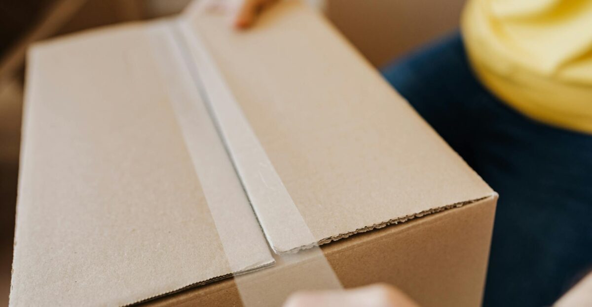 Close-up of a person sealing a cardboard box with tape suggesting relocation or delivery