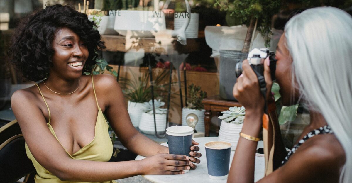 Two friends enjoying coffee outdoors capturing moments with a camera on a sunny day