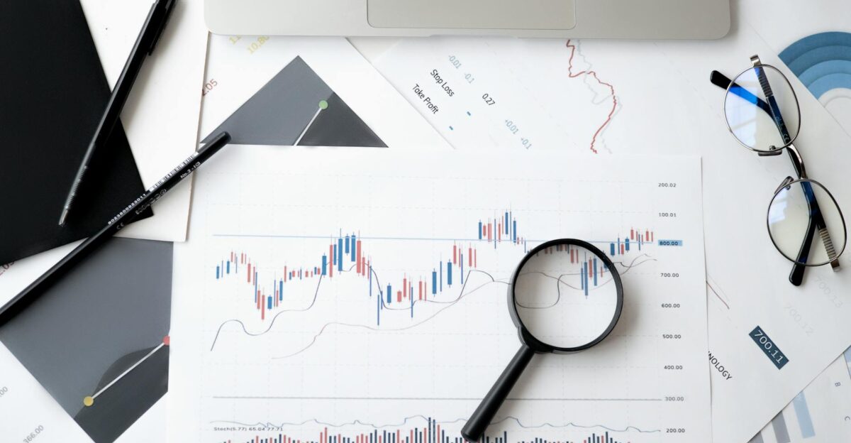 Flat lay of stock market analysis documents with magnifying glass pens and glasses