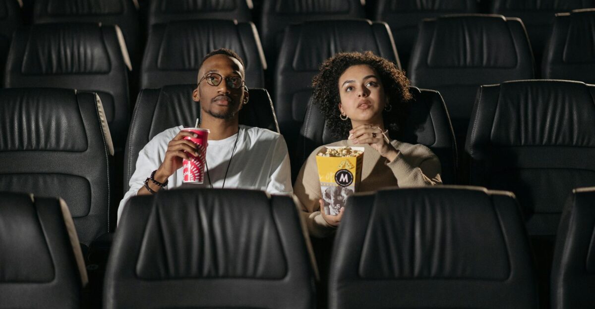 A couple sits in a cinema enjoying popcorn while watching a movie