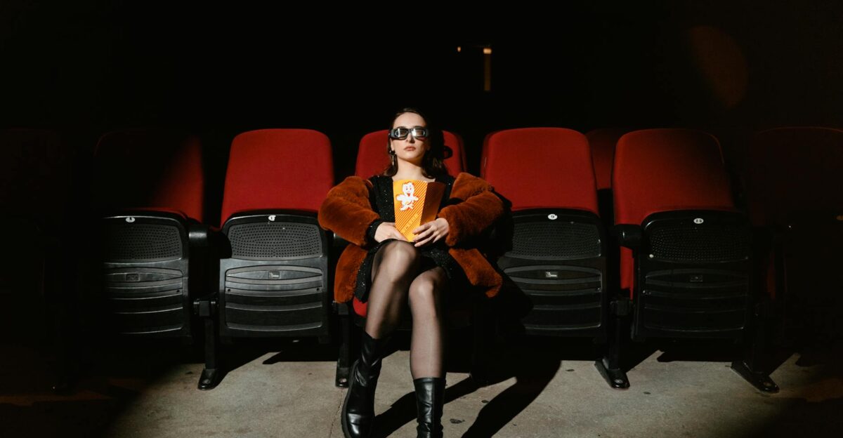 A stylish woman sits alone in a dark cinema enjoying popcorn during a movie