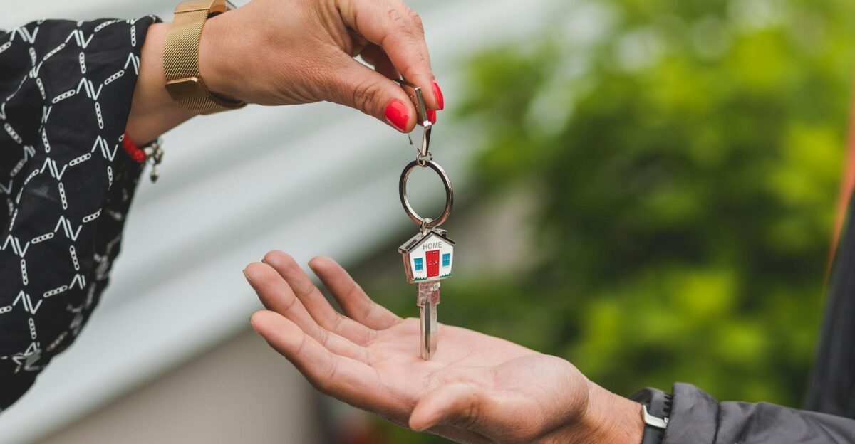 Close-up of a hand handing over a key with a house keychain symbolizing real estate transaction
