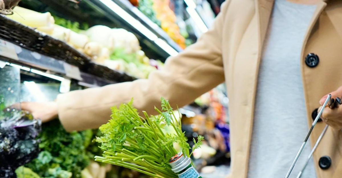 Woman selecting fresh produce in a supermarket with a basket full of groceries