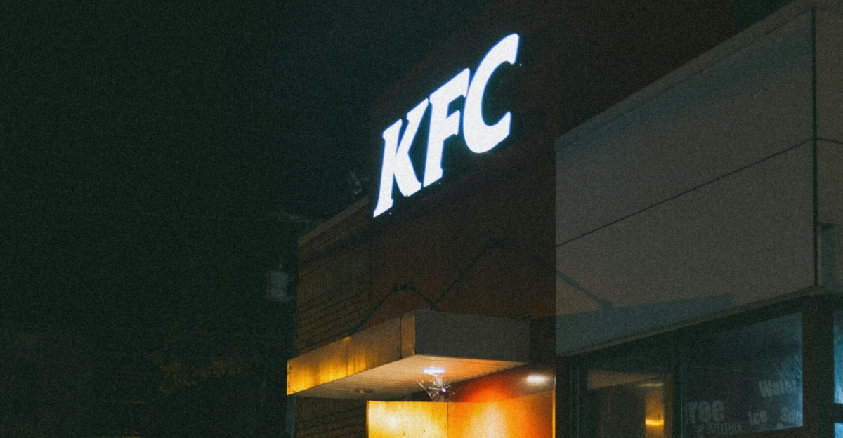 Capture of an illuminated KFC restaurant at night, featuring signage and a quiet street.
