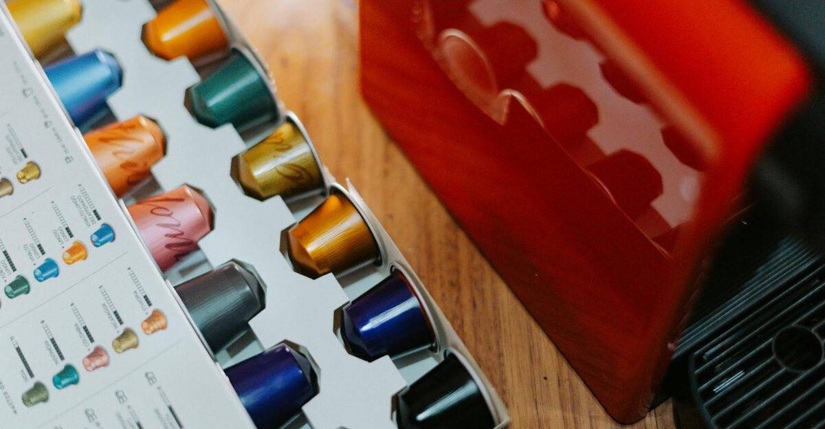 Close-up of colorful coffee capsules next to a coffee machine on a wooden table
