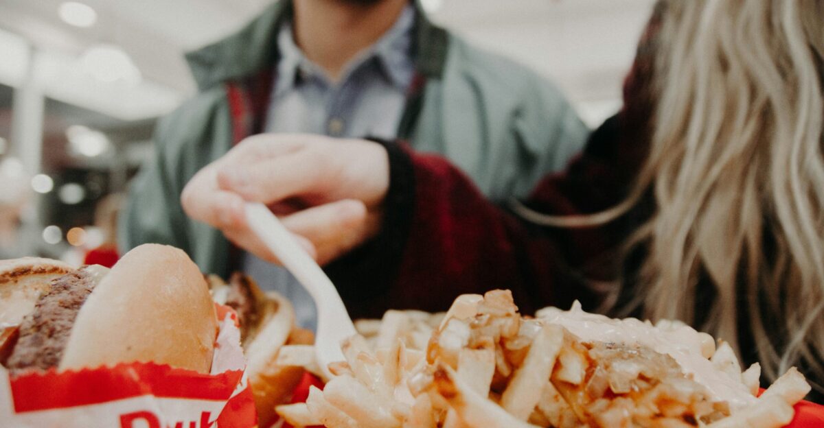 woman in maroon long-sleeved shirt holding fork over fries