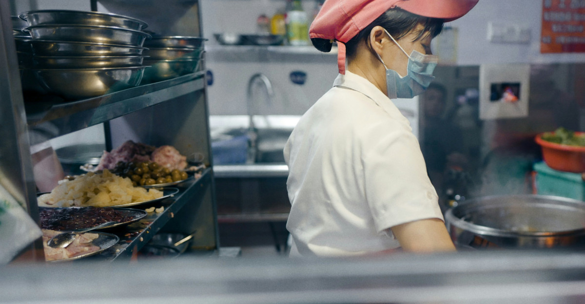 man in white shirt and brown hat standing in front of food counter